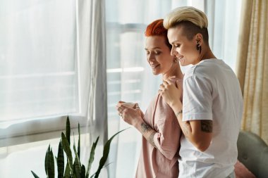 İki kadın, kısa saçlı lezbiyen bir çift, yatak odalarının penceresinin önünde durmuş, mutlu LGBT yaşam tarzlarını sergiliyorlar..