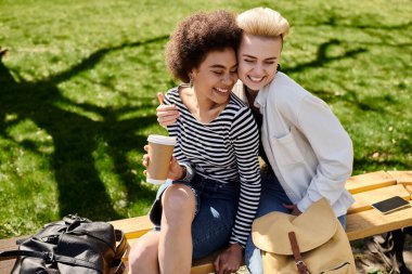 A pair of young women, casually dressed, sitting on a park bench, immersed in conversation and surrounded by lush greenery. clipart