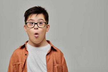 Down sendromlu küçük sevimli bir çocuk gözlük takarken aptalca surat yapıyor..