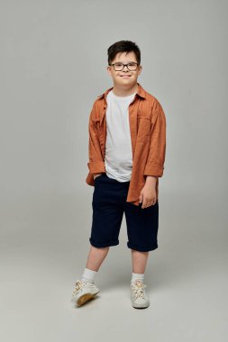 Down sendromlu, gözlüklü ve şortlu bir çocuk portre için poz veriyor.