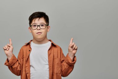 Down sendromlu gözlüklü küçük bir çocuk parmağıyla jest yapıyor..