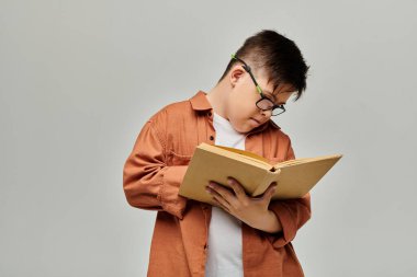 Down sendromlu gözlüklü küçük bir çocuk dikkatle kitap okuyor..