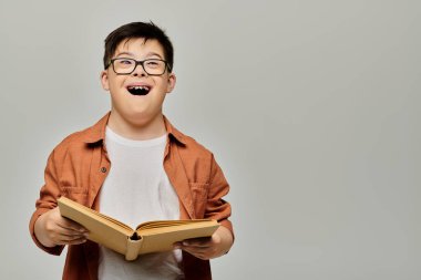 Down sendromlu gözlüklü bir çocuk dikkatle kitap okuyor..