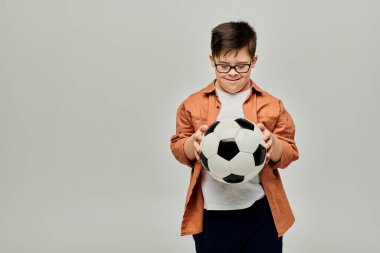 Down sendromlu gözlüklü bir çocuk futbol topu tutuyor.