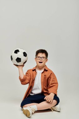 Down sendromlu bir çocuk futbol topunu beyaz arka planda tutuyor..