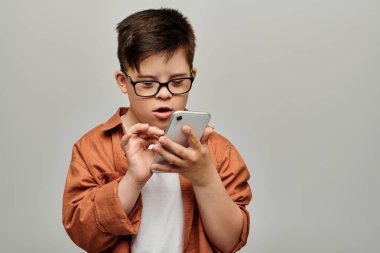 Down sendromlu gözlüklü küçük çocuk dikkatle akıllı telefon ekranına odaklanıyor..
