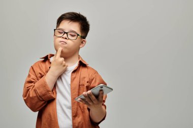 Down sendromlu küçük bir çocuk elinde bir cep telefonu tutuyor, dalgın görünüyor..