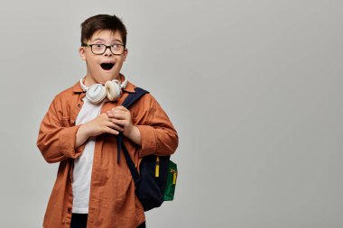 A little boy with Down syndrome with glasses and a backpack explores with curiosity. clipart