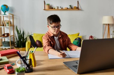 A adorable boy with Down syndrome focused on his laptop at home. clipart