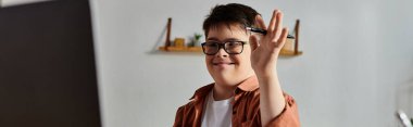 Boy with Down syndrome in glasses waves hand at computer screen. clipart