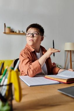 Down sendromlu sevimli bir çocuk elinde kalemle masada oturuyor..