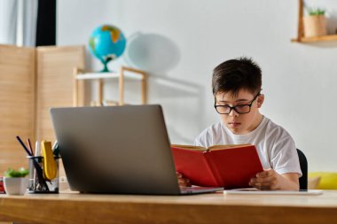 Down sendromlu çocuk masada dizüstü bilgisayarla çalışıyor..