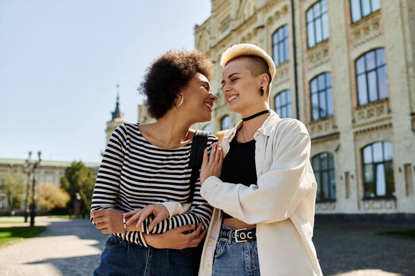 Two stylish young women stand gracefully in front of a modern building on a university campus.