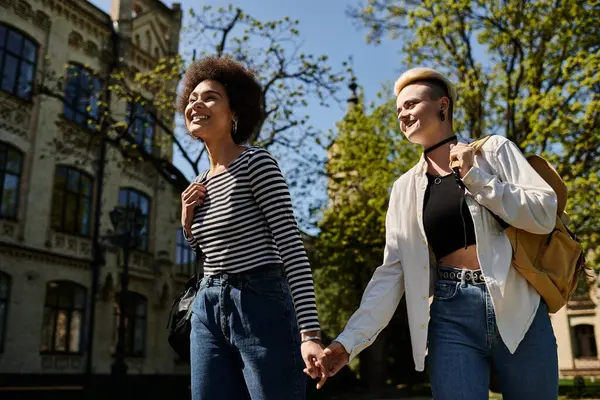 stock image Two young women, a multicultural lesbian couple, walk hand in hand on a university campus.