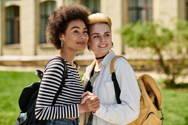 Две молодые женщины в стильных рюкзаках забастовка позирует перед живописным фоном.