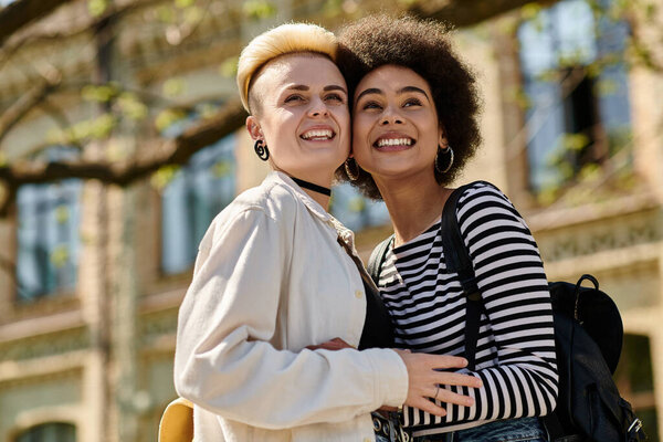 Two young women, multicultural lesbian couple, embracing in front of university building.