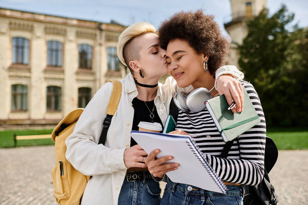 A multicultural lesbian couple in stylish clothing share a tender kiss in front of a building on a university campus.