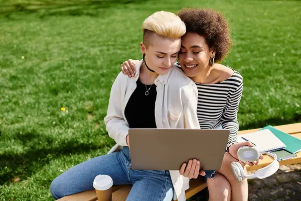 stock image Two young women, seated on a bench, engrossed in a laptop screen, possibly working or studying together.