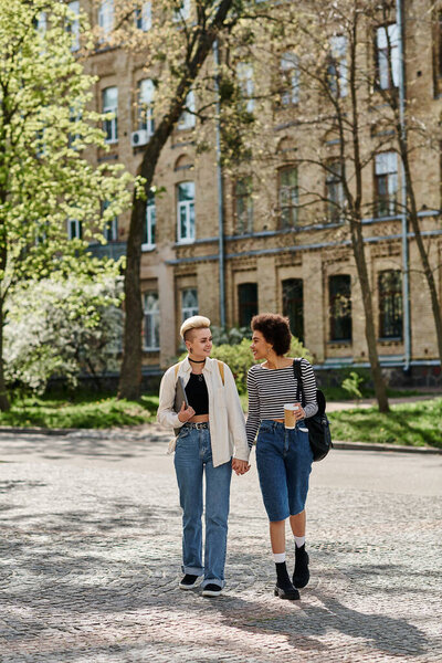 Two young women, a multicultural lesbian couple, strolling down a city street near a university campus in stylish attire.