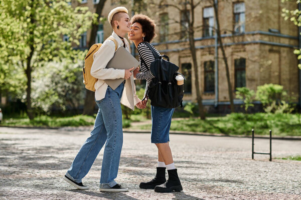 Two young women, a multicultural lesbian couple, stand chatting on a city street by a university campus.