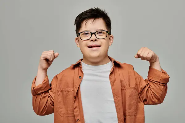 stock image little boy with Down syndrome flexing his arms proudly against a gray background.