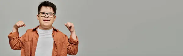 stock image A boy with Down syndrome in glasses exudes confidence with his arms raised in a powerful pose.