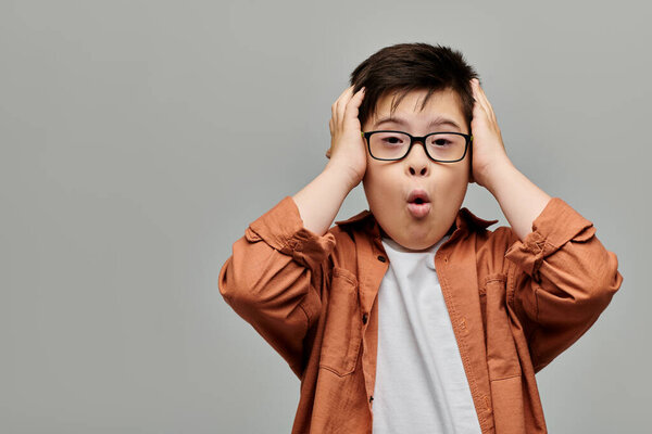 мальчик с синдромом Дауна в очках, с руками на голове.