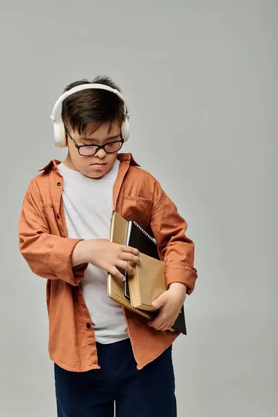 stock image little boy with Down syndrome wearing headphones while holding books.