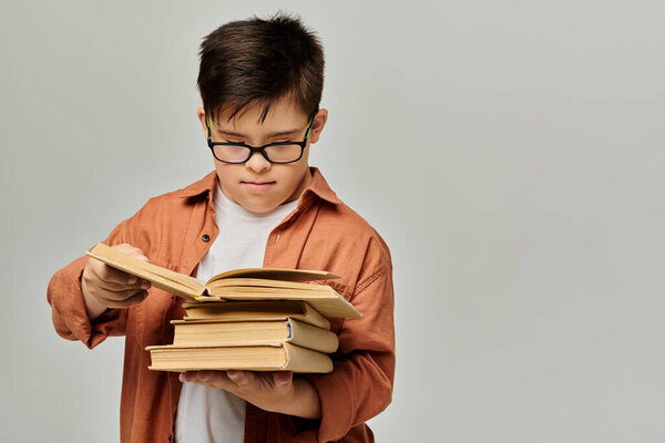 A boy with Down syndrome with glasses holds a stack of books.