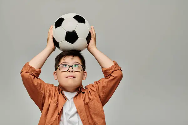 A delightful little boy with Down syndrome joyfully holds a soccer ball above his head.