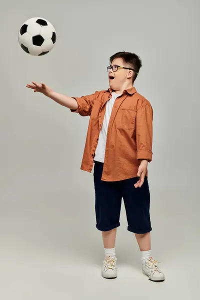 Stock image A little boy with Down syndrome with glasses catches a soccer ball in action.