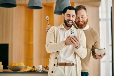 Modern bir apartman dairesinde cep telefonu tutan iki adam mutlu bir şekilde gülümsüyor..