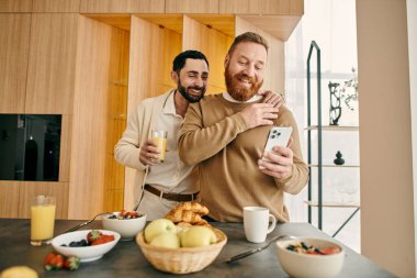 Modern bir mutfakta cep telefonuna bakarken derin sohbetler yapan iki mutlu gay adam..