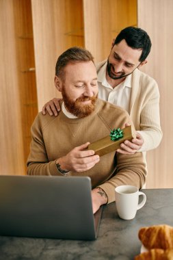 İki adam, modern bir dairede dizüstü bilgisayarın önünde mutluluk ve sevgi dolu bir anı paylaşarak hediyelerini değiş tokuş ederler..