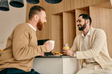 Two men sharing a moment of intimacy and connection as they talk at a table in a modern setting. clipart