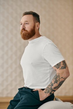 Sakallı, memnun bir adam rahat bir şekilde oturur, modern bir oturma odasında huzur ve rahatlama hissi yayar..