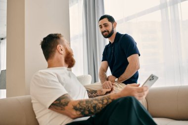 Gündelik giysiler içinde mutlu bir çift oturma odasındaki modern bir kanepede sohbet ediyorlar, LGBTQ sevgi ve bağlarını somutlaştırıyorlar..