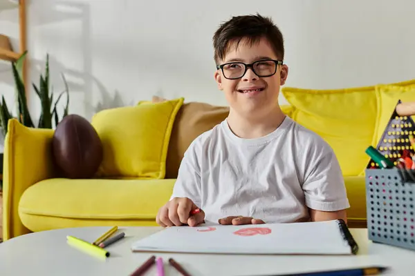 Uroczy Chłopiec Zespołem Downa Okularami Siedzi Przy Stole Otoczony Kolorowymi — Zdjęcie stockowe
