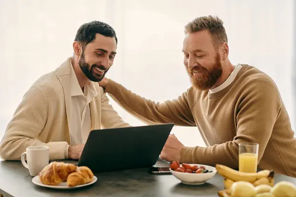 stock image Two men immersed in a laptop screen at a table in a modern setting, engaged in a shared activity.