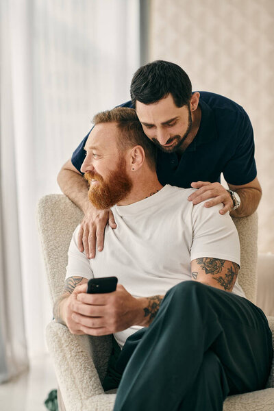 Two men in casual clothes embrace each other warmly on a cozy couch in a modern living room, symbolizing their happy relationship.