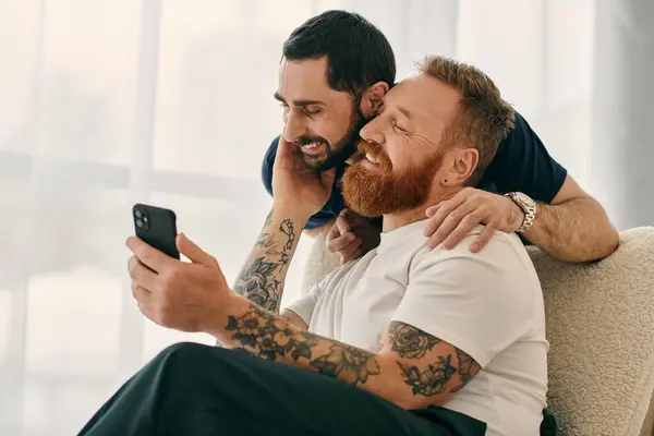 stock image Two men in casual attire sitting on a couch, fully engaged with a cell phone.