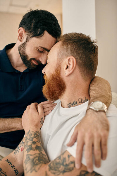 Two men with tattoos on their arms hug each other in a display of love and unity in a modern living room.