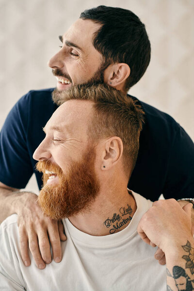 Two men, with tattoos on their arms, share a warm hug in a display of love and affection.