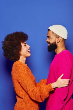 A young African American man and woman, friends in vibrant attire, stand united on a blue background. clipart