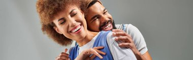 An African American man and woman, friends, embrace in a stylish pose against a grey background. clipart