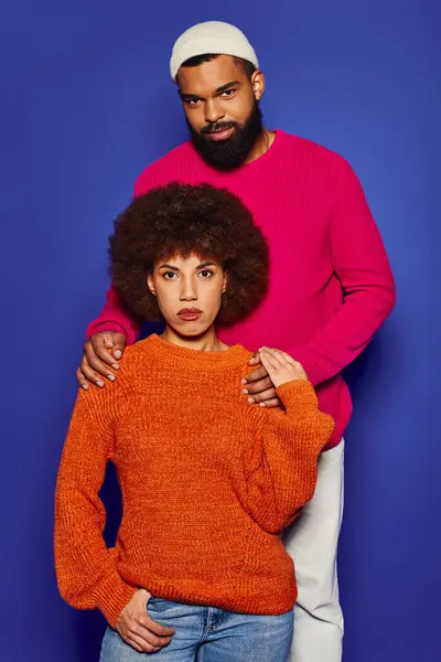 stock image A young African American man and woman, dressed in vibrant casual attire, stand next to each other against a blue background.