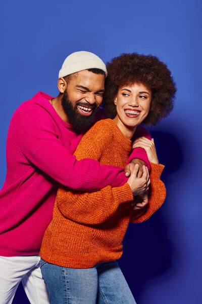 Young African American friends, a man and a woman, in vibrant casual attire embracing each other on a blue background.