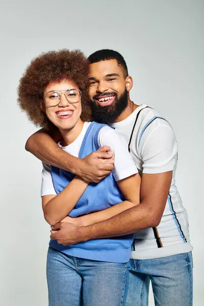 stock image An African American man and woman in stylish clothes embrace each other, symbolizing friendship and connection on a grey background.