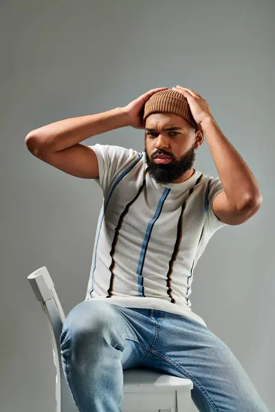 stock image An African American man in stylish clothing sitting on top of a white chair, contemplating with a thoughtful expression.