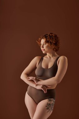 Curvy redhead woman in brown bikini striking a glamorous pose.